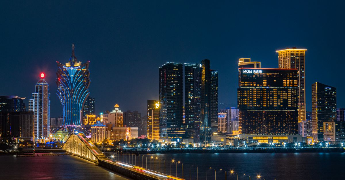 Elegant night view of Macau skyline featuring iconic illuminated hotels and a lit bridge over water.